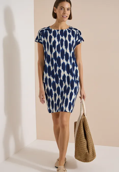 Knielanges Kleid mit Capsleeves und Print urban dark blue Frau in blau-weiß gemustertem kurzärmeligem Kleid mit Korbtasche.