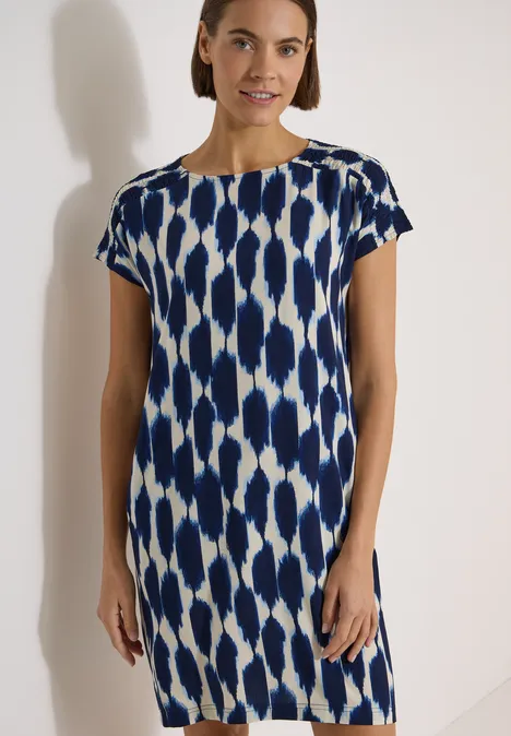 Knielanges Kleid mit Capsleeves und Print urban dark blue Frau steht vor neutralem Hintergrund in knielangem, kurzärmeligem blau-weiß gemusterten Kleid.