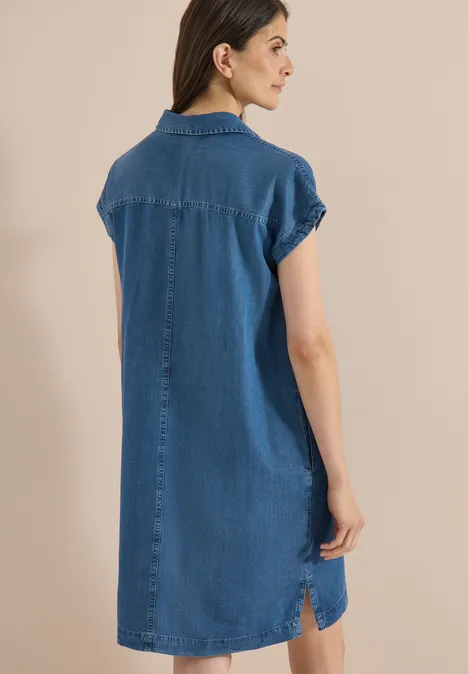 Frau von hinten in locker sitzendem Jeans-Hemdkleid mit kurzen Ärmeln vor neutralem Hintergrund.