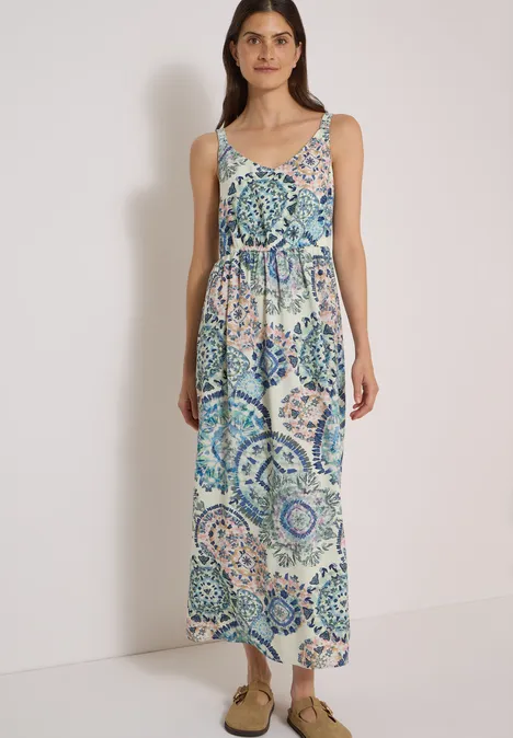 Frau in ärmellosem Maxikleid mit blau-grünem Mosaikmuster und Spaghettiträgern, dazu Sandaletten.