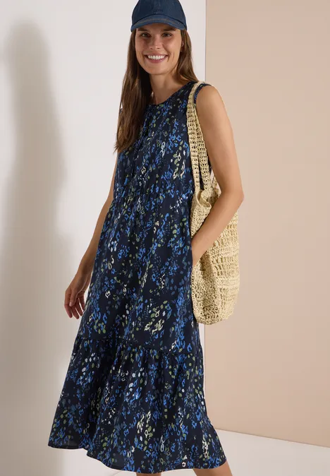 Midikleid mit Split Neck und Print urban dark blue Frau in blauem geblümtem Maxikleid, mit Schirmmütze und Basttasche lächelt