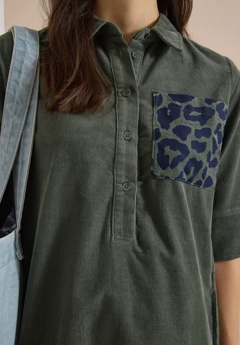 Frau trägt olivgrüne Hemdbluse mit 3/4-Ärmeln, Brusttasche im dunkelblauen Leopardenprint und hellblauem Denim-Beutel.