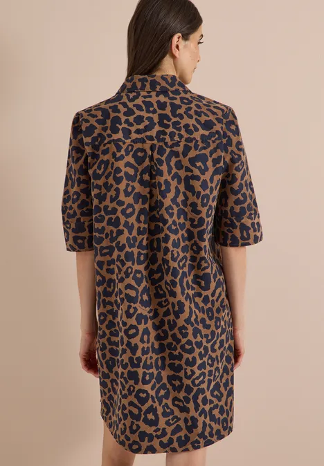 Frau mit schulterlangem Haar trägt Hemdkleid im Leopardenmuster.
