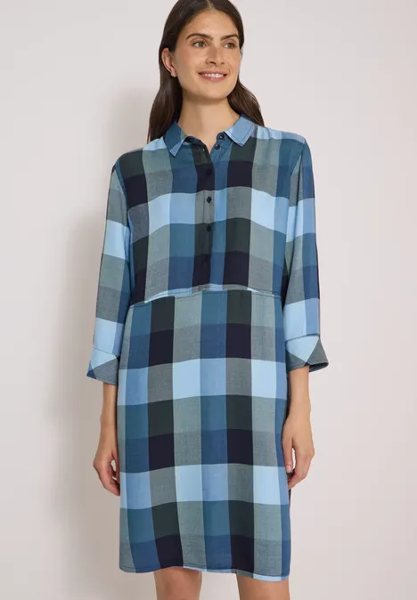 Eine Frau trägt ein blau kariertes Hemdblusenkleid mit 3/4-Ärmeln.