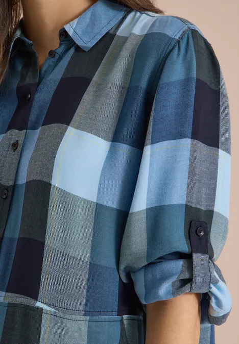 Naheinstellung eines karierten Hemdblusenshirts in Blautönen mit hochgekrempelten Ärmeln.