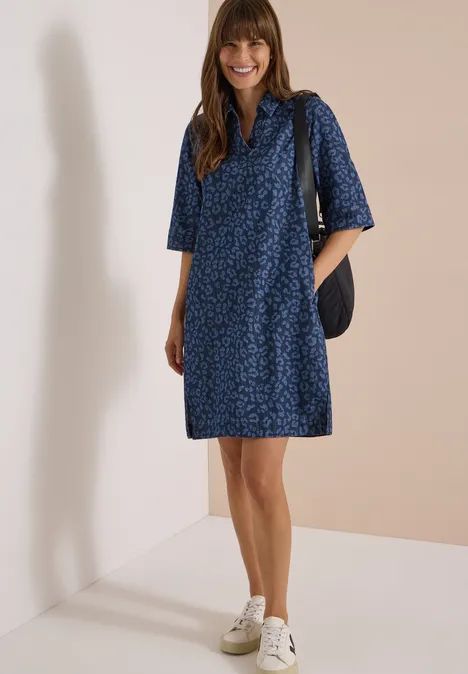 Kniehoge jurk met luipaardprint Dark blue wash Lachende vrouw in knielange donkerblau bloemjurk en witte sneakers voor een lichte achtergrond.