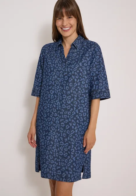 Kniehoge jurk met luipaardprint Dark blue wash Vrouw draagt een losvallende blauwe overhemdjurk met subtiele luipaardprint, kraag, driekwartmouwen en zijsplitten.