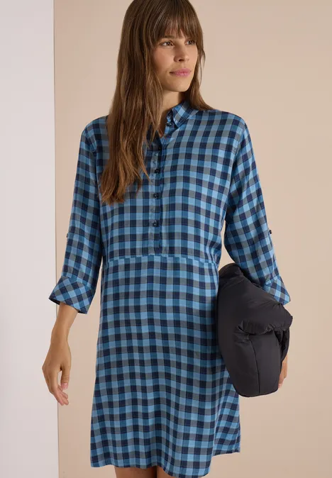 Knie-lange jurk met een fijn ruitjespatroon easy blue Frau in blau-schwarz kariertem Hemdblusenkleid hält in der Hand ein dunkles Kissen.
