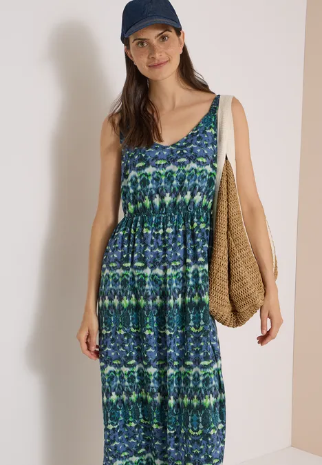 Maxikleid mit V-Neck und Print urban dark blue Frau in blau-grün gemustertem ärmellosem Maxikleid mit Tasche und Cap vor neutralem Hintergrund.