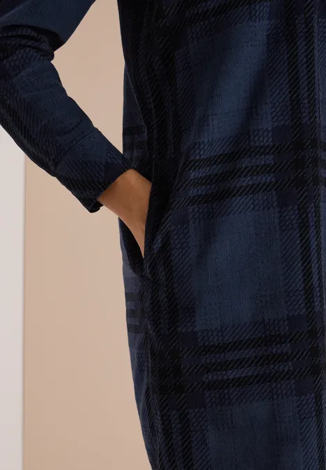 Langärmliges, dunkelblaues, kariertes Kleid mit seitlicher Tasche und Hand darin.