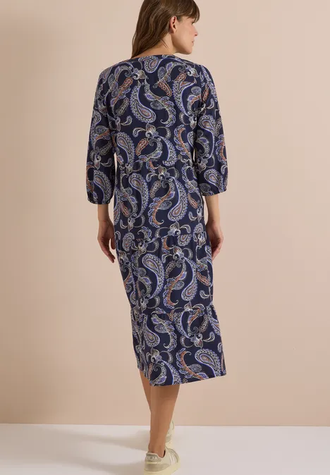 Rückenansicht einer Frau in einem midi Paisley-Kleid mit 3/4-Ärmeln vor beigem Hintergrund.