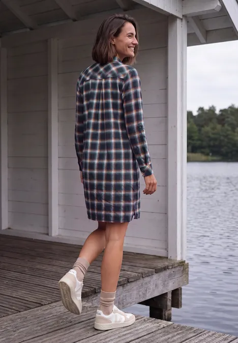 Knielanges Kleid mit Karomuster urban dark blue Frau in kariertem Hemdblusenkleid steht auf Steg und blickt über ruhigen See.