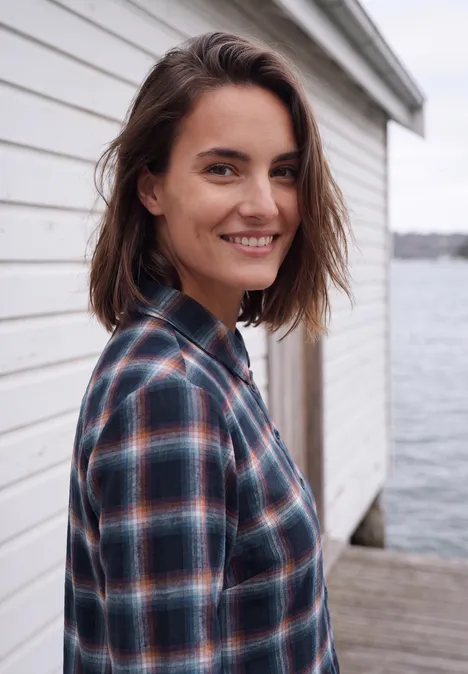 Knielanges Kleid mit Karomuster urban dark blue Eine lächelnde Frau in karierter Bluse lehnt an einer weißen Holzwand am Wasserpier.