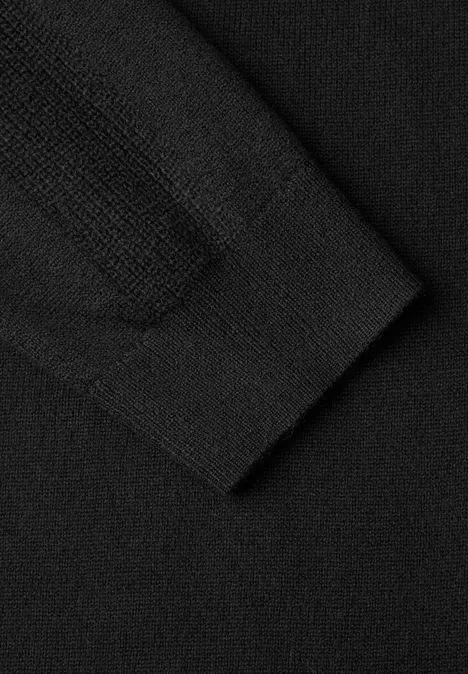Nahaufnahme eines schwarzen Strickpullovers mit sichtbarer Ärmelsaum-Naht und feiner Struktur.