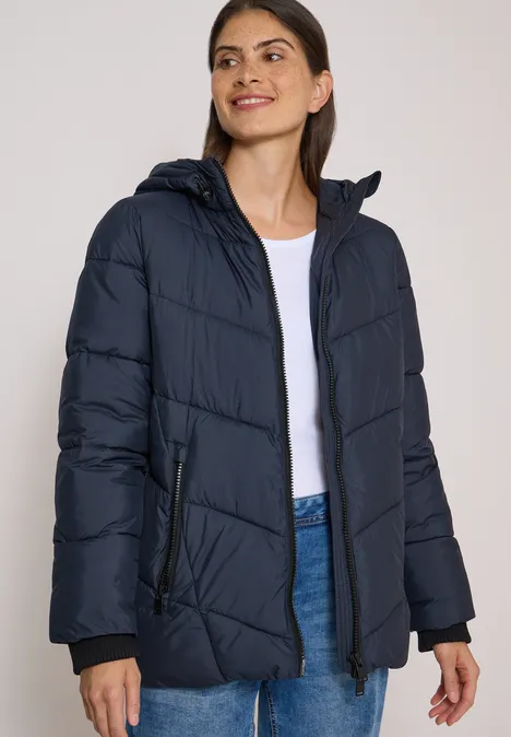 Puffer-Jacke in Midi-Länge mit Kapuze dark navy blue Frau in dunkelblauer Steppjacke, weißem Shirt und Jeans.