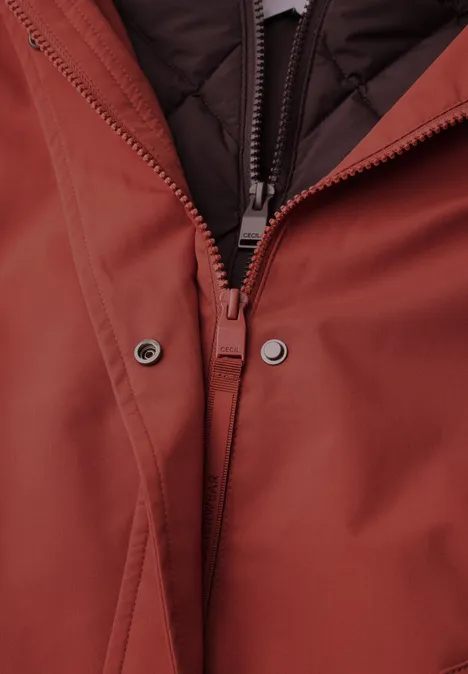 2-in-1-jas met gewatteerd vest als inzetstuk light russet red Close-up van de ritssluiting van een roestkleurige jas met drukknoopsluiting en doorgestikte voering.