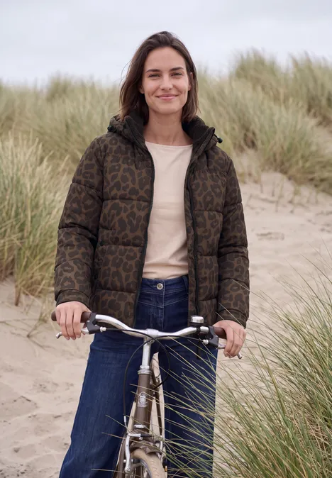 Steppjacke mit Kapuze und Reißverschluss dark toffee brown Eine lächelnde Frau mit Fahrrad in einer Dünenlandschaft, trägt Daunenjacke, Jeans und T-Shirt.
