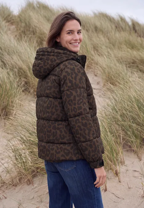 Steppjacke mit Kapuze und Reißverschluss dark toffee brown Frau in brauner, gemusterter Daunenjacke steht lächelnd in Dünenlandschaft.