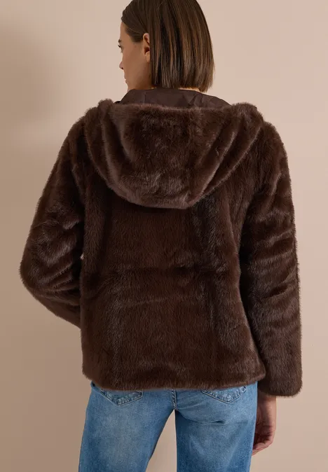 Frau von hinten in brauner, flauschiger Jacke mit Kapuze und Jeans.