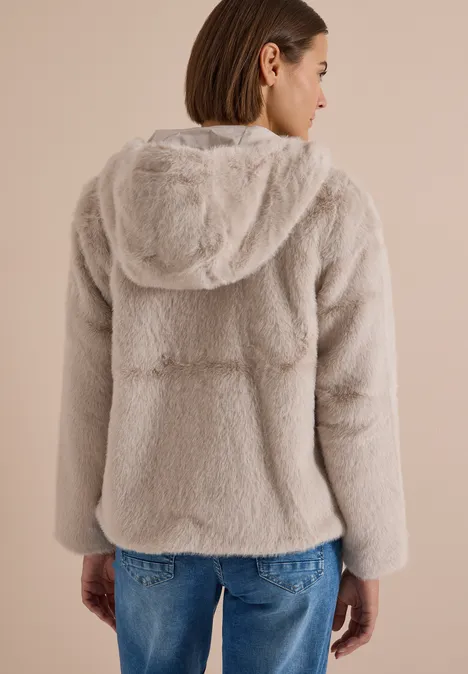 Frau trägt hellbeige flauschige Kapuzenjacke, Rückenansicht, kombiniert mit blauen Jeans.