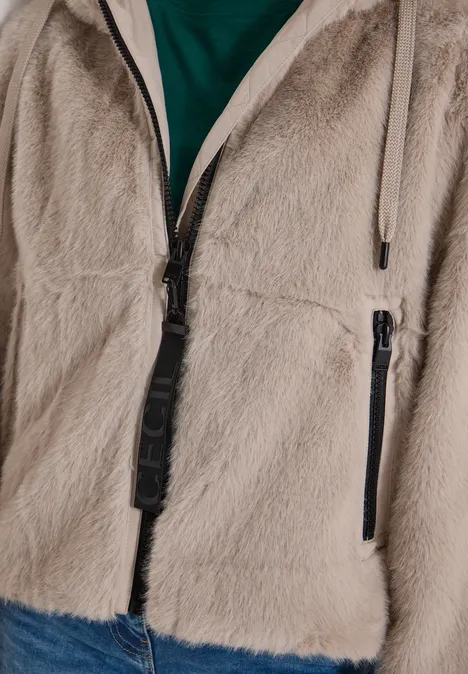 Nahaufnahme einer beigen, flauschigen Fleecejacke mit Reißverschluss und Tasche, darüber ein grünes Shirt.