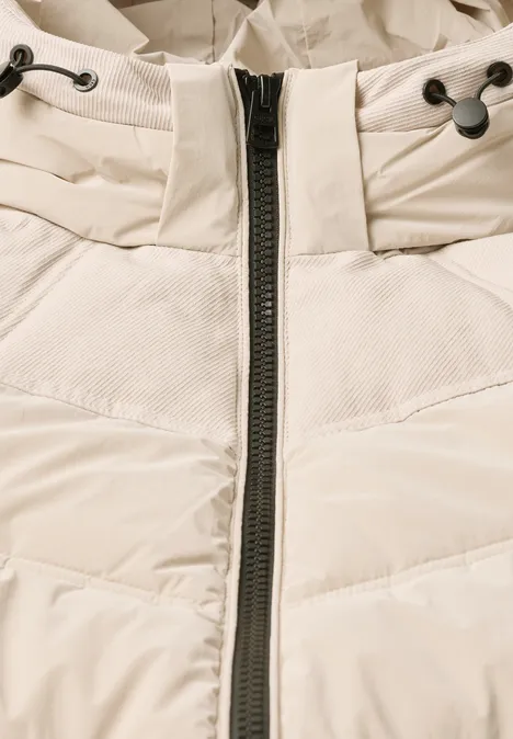 Nahaufnahme einer cremefarbenen, gesteppte Winterjacke mit Reißverschluss und Kordelzug am Kragen.