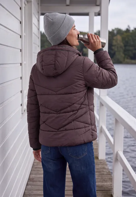 Veste matelassée à capuche et fermeture zip berry red Femme en veste matelassée et bonnet boit d’une bouteille sur un ponton au bord de l’eau.