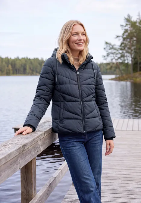 Steppjacke mit Kapuze und Zipper dark navy blue Eine lächelnde Frau in schwarzer Steppjacke und Jeans steht auf einem Steg am See im Wald.