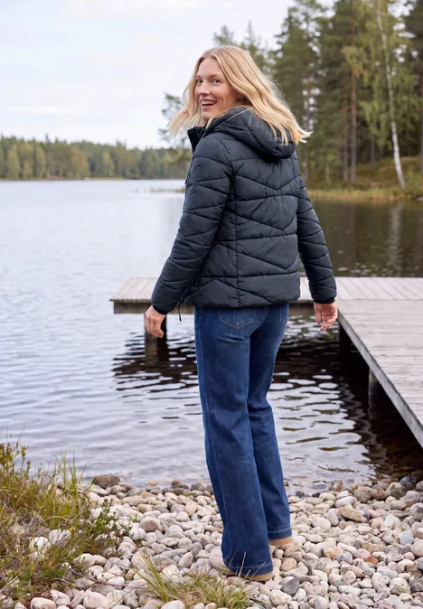 Steppjacke mit Kapuze und Zipper dark navy blue Eine Frau in schwarzer Steppjacke und Jeans lächelt am ruhigen Seeufer neben einem Holzsteg im Wald.