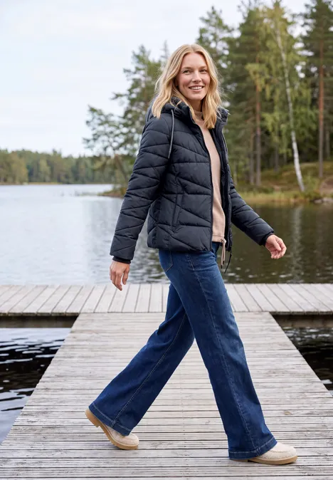 Steppjacke mit Kapuze und Zipper dark navy blue Eine Frau spaziert lächelnd auf einem Steg am See, trägt schwarze Jacke und Jeans.