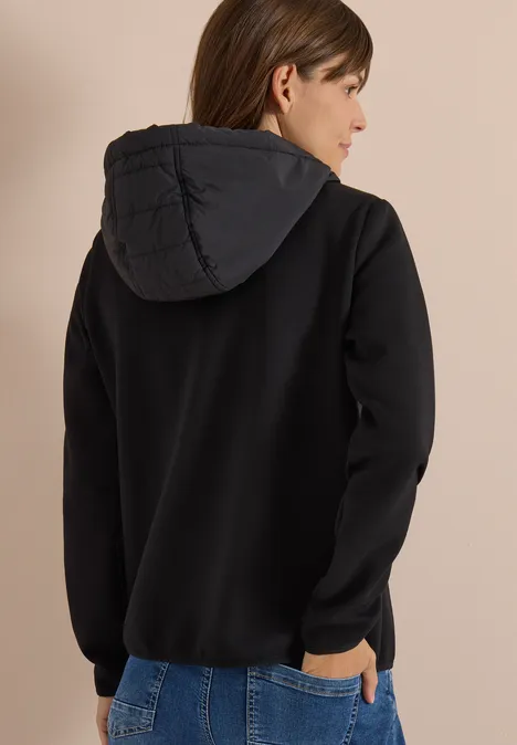 Une personne vue de dos porte un sweat à capuche noir et un jean bleu.