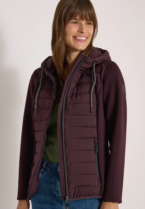 Femme souriante portant une veste bordeaux à capuche.