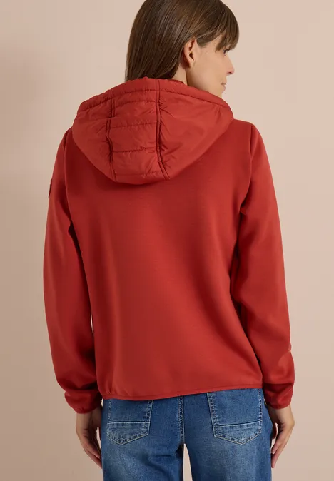 Vue de dos d'une femme portant un sweat à capuche rouge matelassé et un jean.