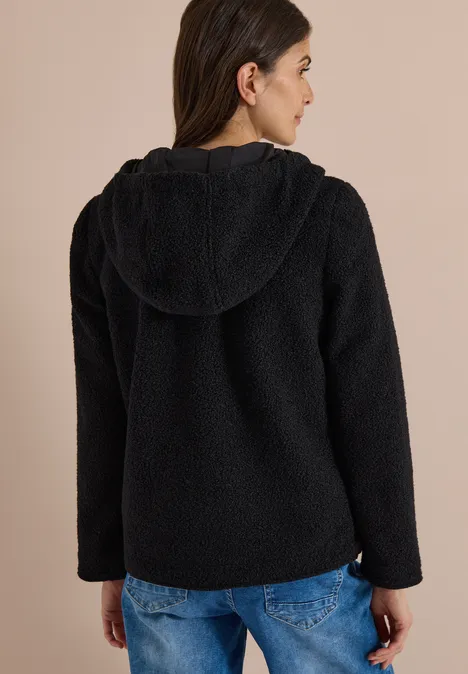 Frau von hinten in schwarzer, flauschiger Kapuzenjacke und blauen Jeans