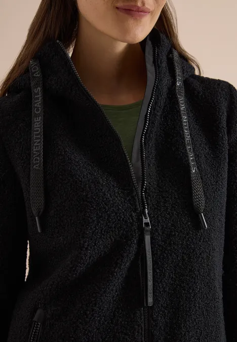 Nahaufnahme einer Frau in schwarzem Fleece-Jacke mit Reißverschluss und grünem Shirt.