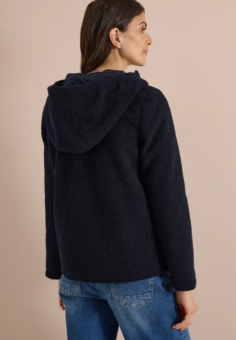 Femme de dos portant une veste en polaire teddy bleu marine à capuche et un jean.
