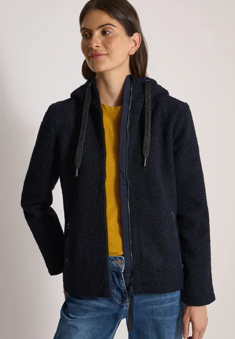 Femme portant une veste polaire bleue marine à capuche, un t-shirt jaune et un jean.