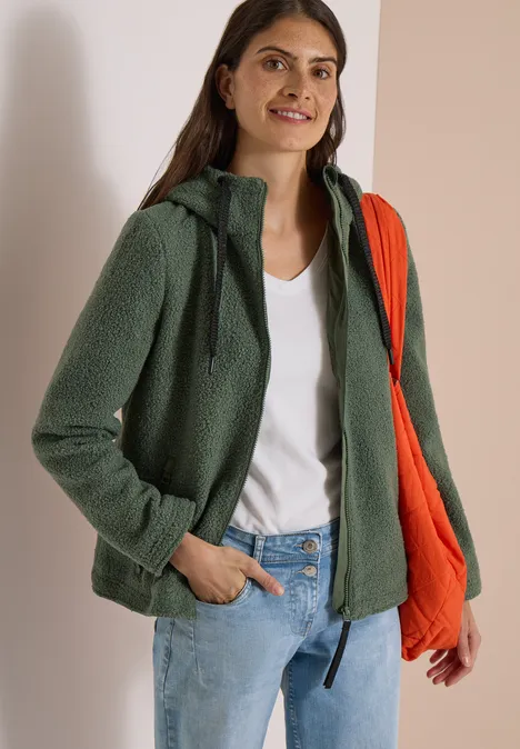 Jeune femme en veste polaire verte, top blanc, jean bleu et sac bandoulière orange.