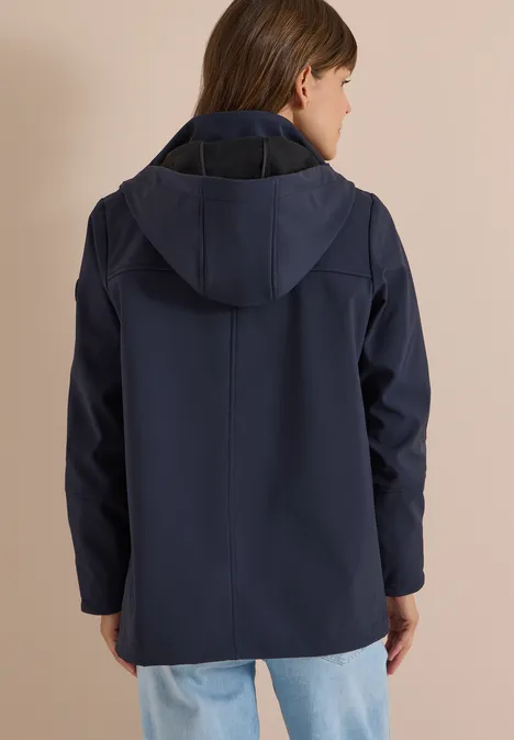 Eine Person von hinten trägt eine dunkelblaue Jacke mit Kapuze vor beigem Hintergrund.