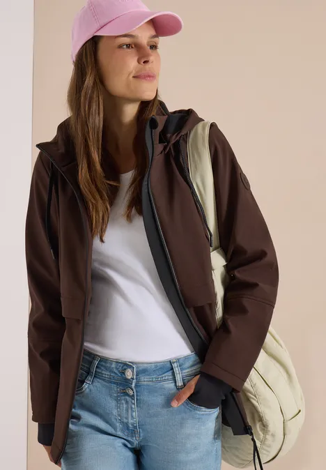 Jeune femme portant une casquette rose, veste marron, t-shirt blanc, jean et sac à dos.