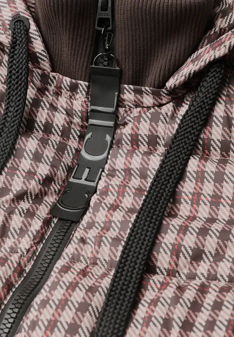 Close-up van een jas met bruin-witte pied-de-pouleprint, zwarte ritssluiting en koordjes.