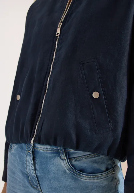 Dunkelblaue Jacke mit Reißverschluss und blaue Jeans, nur Oberkörper sichtbar.