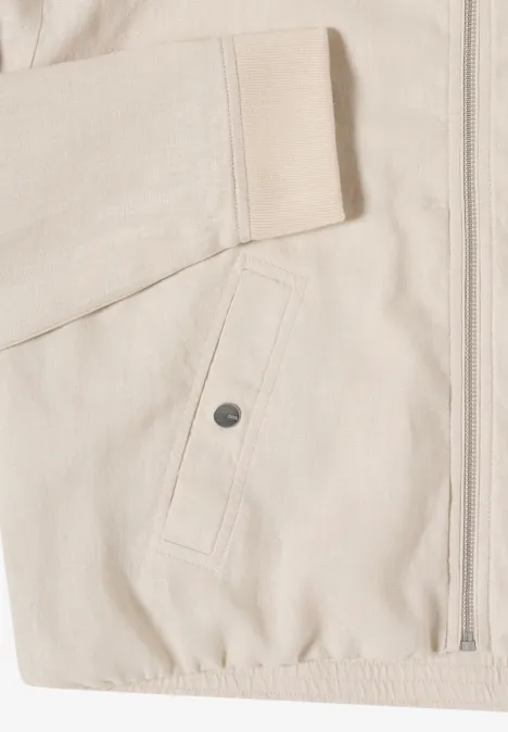 Close-up van een lichtbeige jas met rits, opgestikte zak met drukknop en elastische zoom.