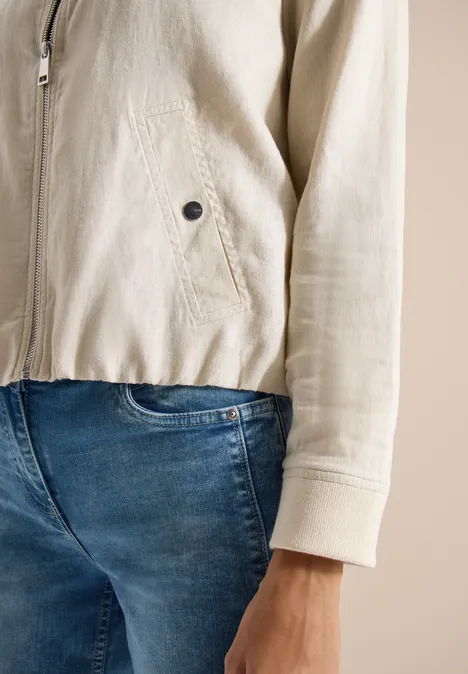 Close-up van iemand in lichtbeige jas en blauwe spijkerbroek, focus op romp en hand.