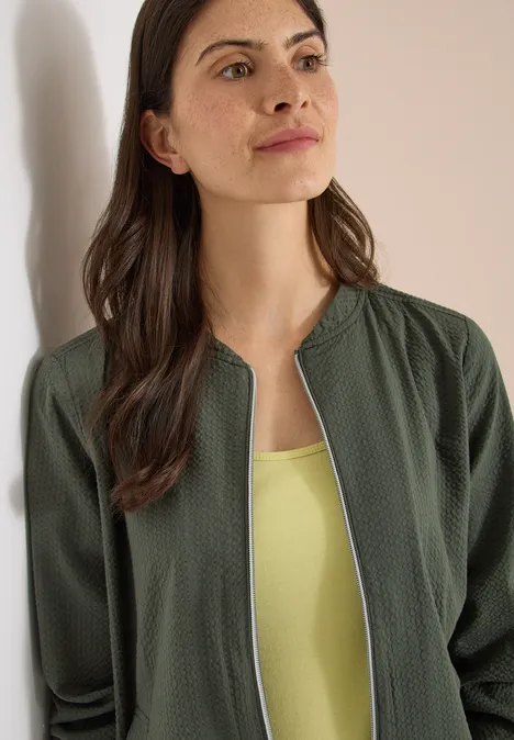 Frau trägt olivgrünen Cardigan mit Reißverschluss über hellgrünem Top.