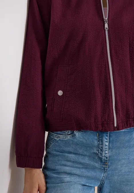 Blouson in Seersuckerqualität mit Zipper sweet grape red Bordeauxroter Reißverschluss-Blouson mit Strukturstoff und aufgesetzten Taschen, kombiniert mit blauen Jeans.