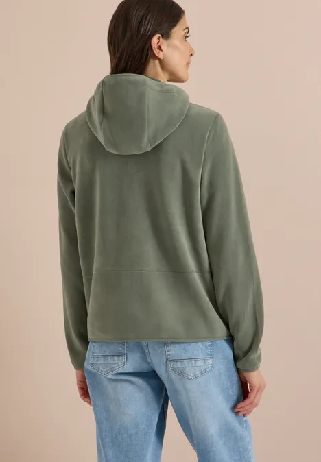 Frau von hinten in grüner Kapuzenjacke und Jeans, blickt leicht zur Seite