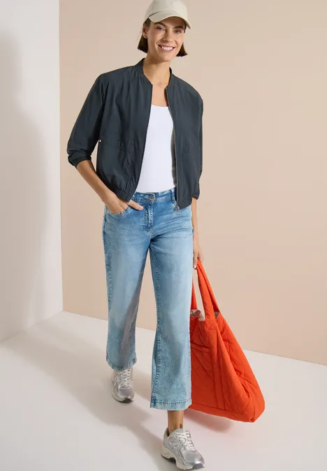 Blouson in Unifarbe mit Zipper palm breeze green Frau in schwarzer Jacke, weißem Top und weitem Jeans, silbernen Schuhen, große rote Tasche tragend.