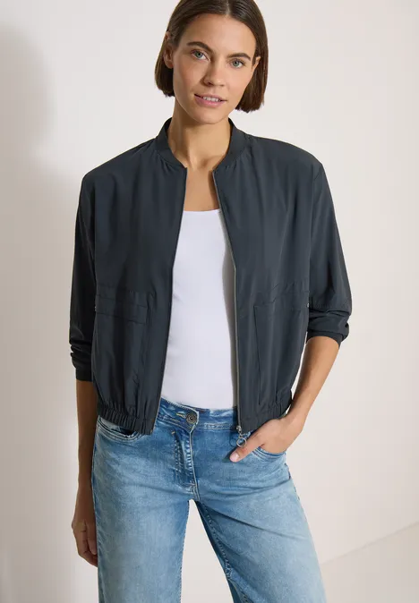 Blouson in Unifarbe mit Zipper palm breeze green Frau trägt dunkle Bomberjacke, weißes Top und blaue Jeans.