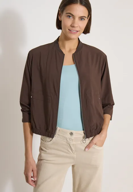 Blouson in Unifarbe mit Zipper brown cacao Frau in brauner Leichtjacke, hellblauem Top und beiger Hose, Hände in den Taschen.